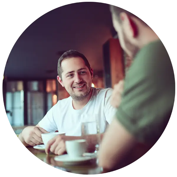 Men engaging in conversation over coffee in a warm café setting, illustrating connection and support during challenging times.