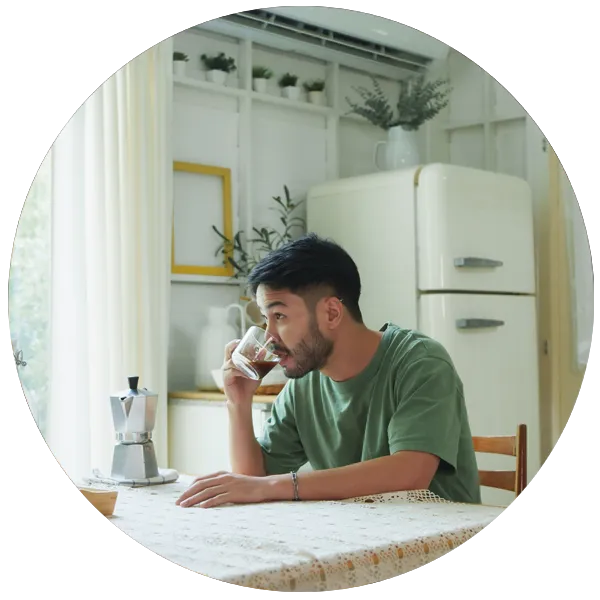 Man enjoying a cup of coffee at a table in a bright kitchen, emphasising daily self-care habits for mental wellbeing.