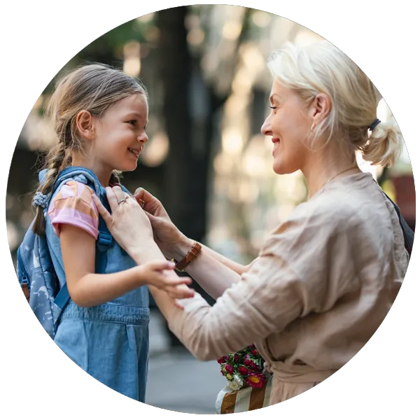 Woman assisting young girl with backpack in an outdoor setting, highlighting nurturing relationships and support, reflecting themes of autonomy and mental wellbeing for self-employed individuals.