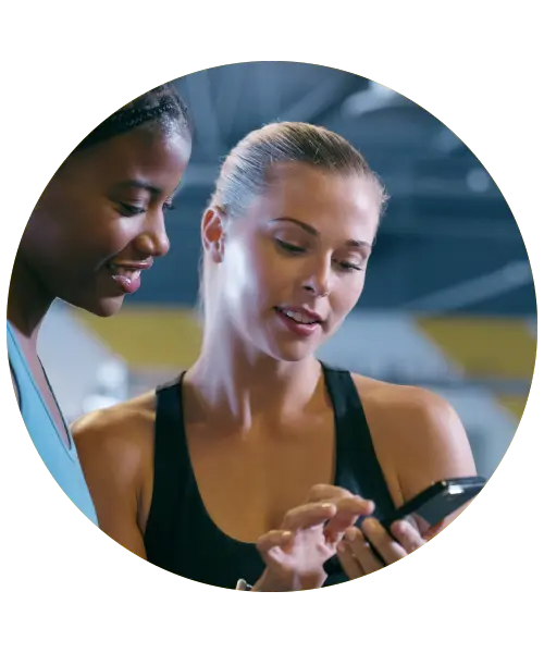Two women in a gym looking at a smartphone, illustrating Tidy app's features for self-employed professionals managing schedules and payments.