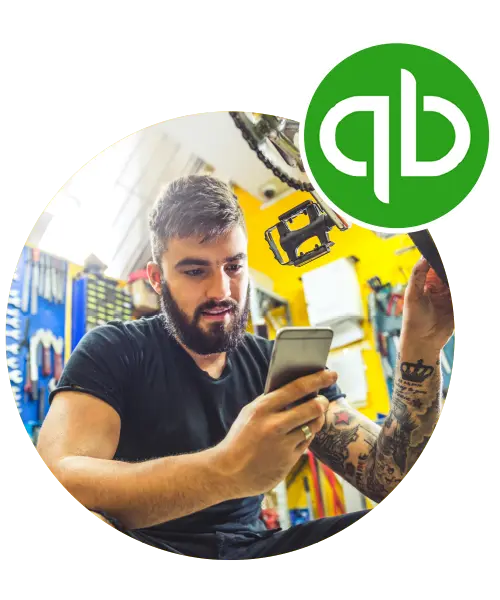 Man with tattoos checking smartphone in workshop, QuickBooks logo in corner, illustrating Tidy's integration with QuickBooks for streamlined business management.