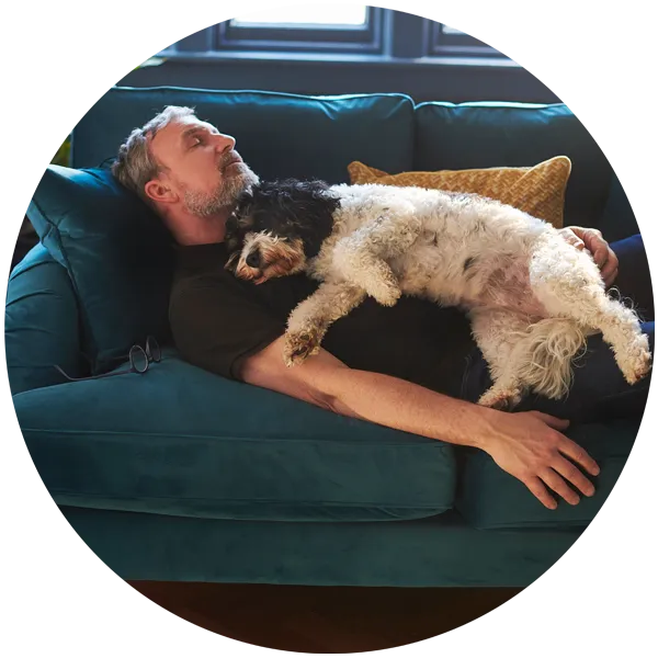 Man resting on a teal sofa with a dog peacefully lying on his chest, illustrating the importance of relaxation and self-care for mental health.