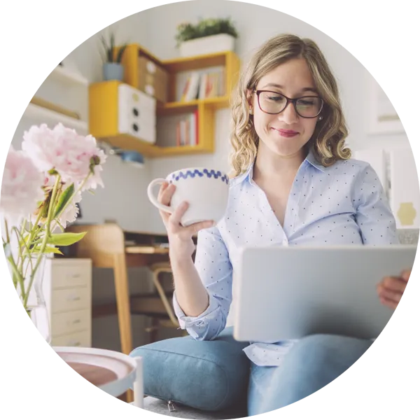 Woman holding a cup and using a tablet in a bright, comfortable home office, surrounded by flowers, emphasising self-care and productivity for self-employed individuals.